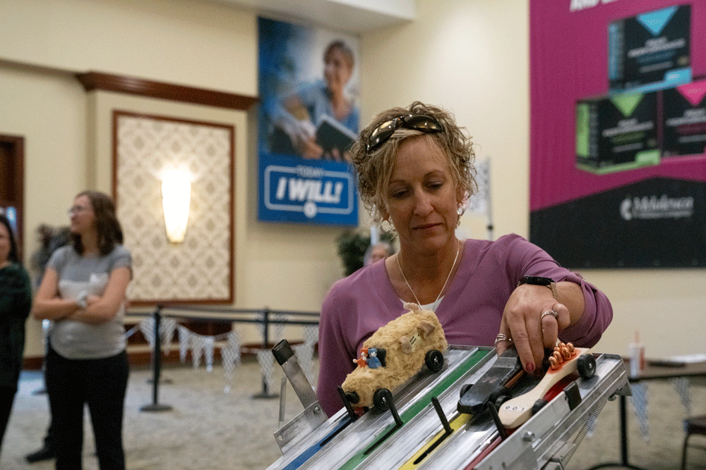 women placing a car on Melaleuca pinewood derby tract